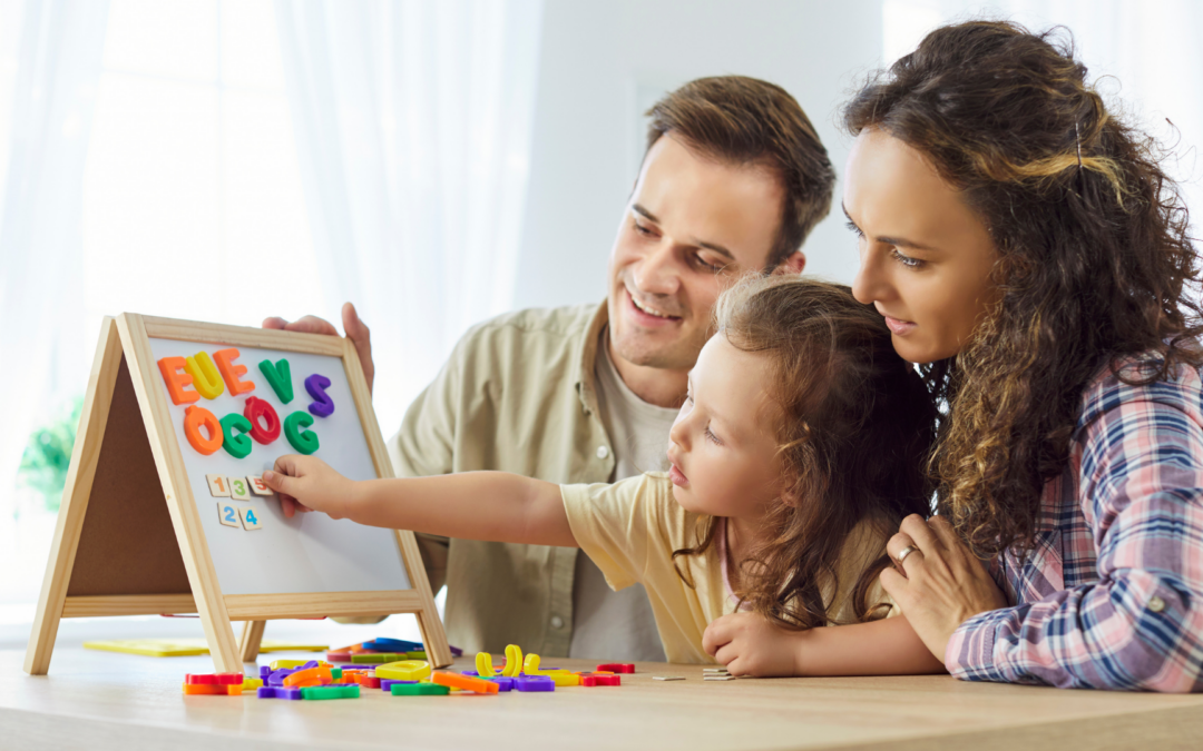 Family of three learning together at a table with a small magnetic letter board and colorful letters, smiling at the activity.