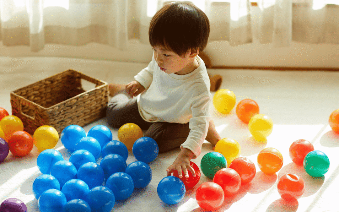 Toddler playing with colorful plastic balls on a sunlit floor, showing the importance of routine for toddlers
